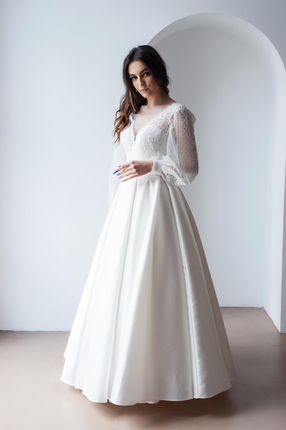 Schöne attraktive Braut im Hochzeitskleid mit weißem Hintergrund des langen vollen Rockes