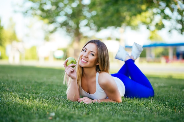 Schöne attraktive junge Frau, die Apfel isst und draußen genießt. Gesundes Lebensstilkonzept.