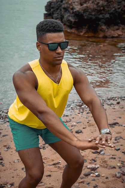 Schöne Aufnahme eines jungen Mannes mit Sonnenbrille, der Übungen mit dem See im Hintergrund macht