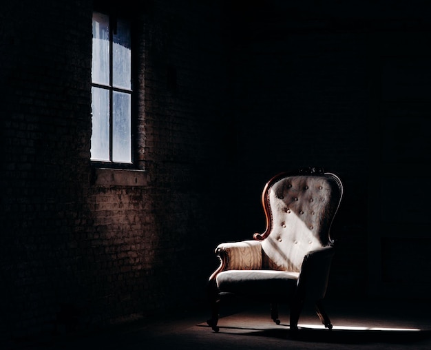 Schöne Aufnahme eines Retro-Stuhls im dunklen leeren Raum mit einem Streifen Fensterlicht, der darauf fällt