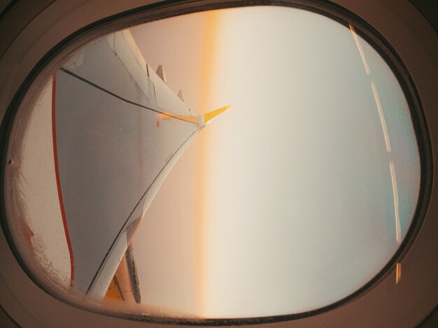 Schöne Aussicht auf den Sonnenuntergang auf Wolken und Himmel durch das Flugzeugfenster mit Flügel gesehen. Fliegen und reisen. Blick auf Himmel und Flügel von der Innenseite des Flugzeugfensters