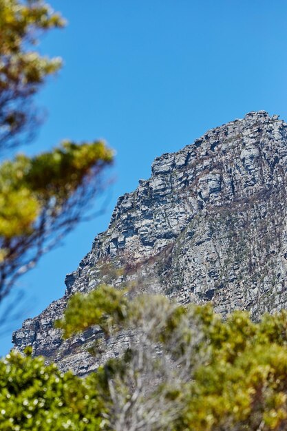 Schöne Aussicht auf einen Berg und einen blauen Himmel mit grüner Natur und Kopierraum von unten Malerischer und ruhiger Berggipfel oder Gipfel mit felsiger Landschaftsansicht eines abgelegenen Ortes an einem sonnigen Sommertag