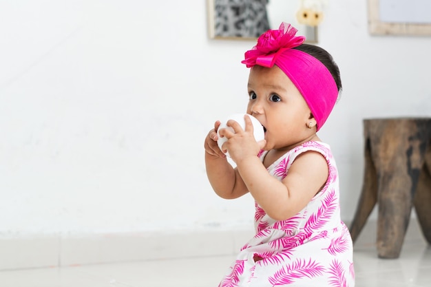 Schöne Baby-Brünette, die auf dem Boden sitzt und mit einem Ball spielt, weißer Hintergrund im Wohnzimmer