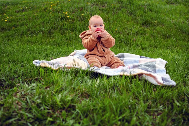 Foto schöne baby-mädchen sitzt auf einem plaid und isst einen apfel auf dem grünen rasen