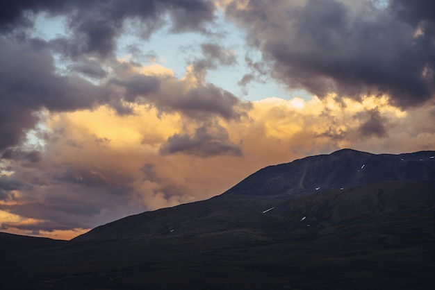 Schöne Berglandschaft mit goldenem Morgenlicht bei bewölktem Himmel. Malerische Berglandschaft mit leuchtender Farbe im Sonnenuntergangshimmel. Silhouetten von Bergen bei Sonnenaufgang. Gold leuchtendes Sonnenlicht im Himmel