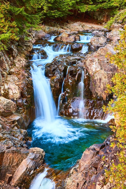 Schöne blaue Wasserfälle, die sich in Eimer mit Felsen ergießen, umgeben von Wald