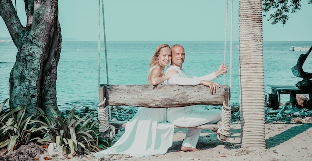 Schöne blonde Braut im weißen Hochzeitskleiderstand auf Seeufer. Tropisches Meer und Felsen auf dem Hintergrund. Sommerferien-Konzept.