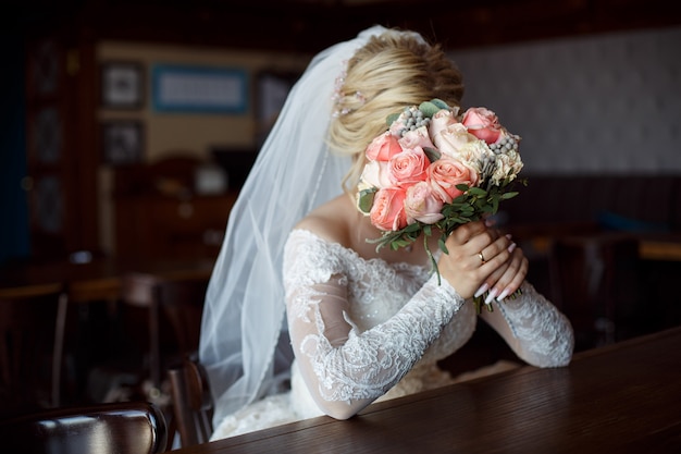 schöne blonde Braut mit einem Blumenstrauß von Rosen Innen. Hochzeitstag . lustiges Porträt eines stilvollen Brautabschlusses oben