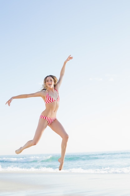 Schöne blonde Frau, die auf den Strand springt