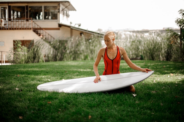 Schöne blonde Frau, die auf grünem Rasen mit einem Wakeboard sitzt