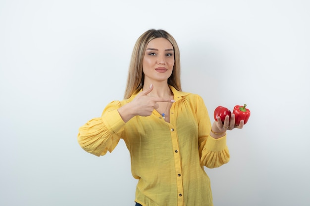 Schöne blonde Frau, die auf rote Paprika zeigt