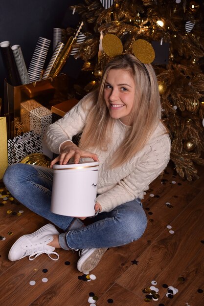 Schöne blonde Frau, die eine Schachtel mit einem Weihnachtsgeschenk in den Händen hält und glücklich lächelt