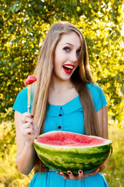 Schöne blonde Frau, die eine Wassermelone im Freien isst