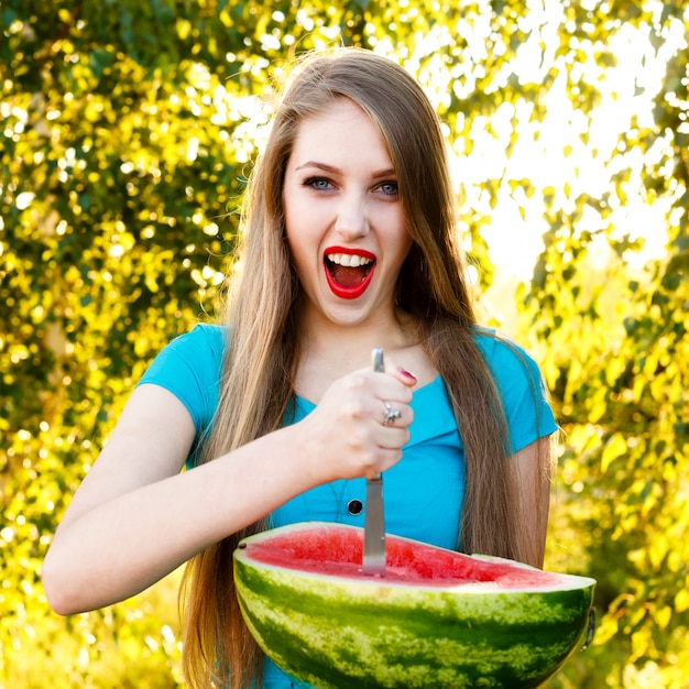 Schöne blonde Frau hält eine Hälfte der Wassermelone