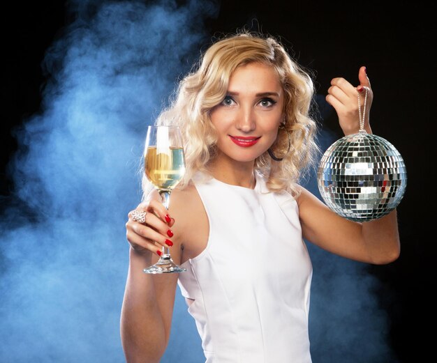 Schöne blonde Frau im Abendkleid mit Wein und Discokugel