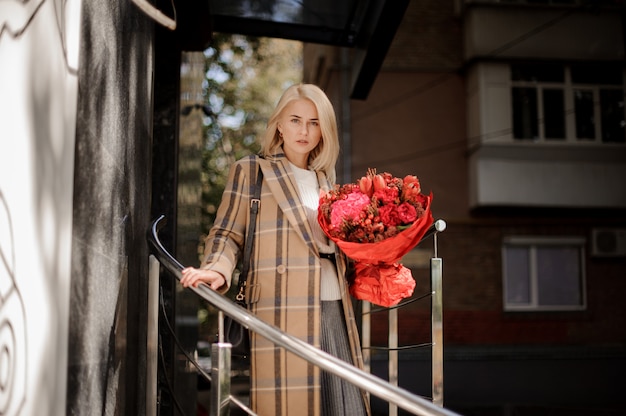 Schöne blonde Frau im karierten Mantel mit einem großen roten Blumenstrauß