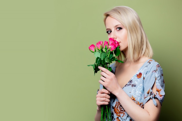 Schöne blonde Frau im Kleid mit Rosen auf grüner Wand