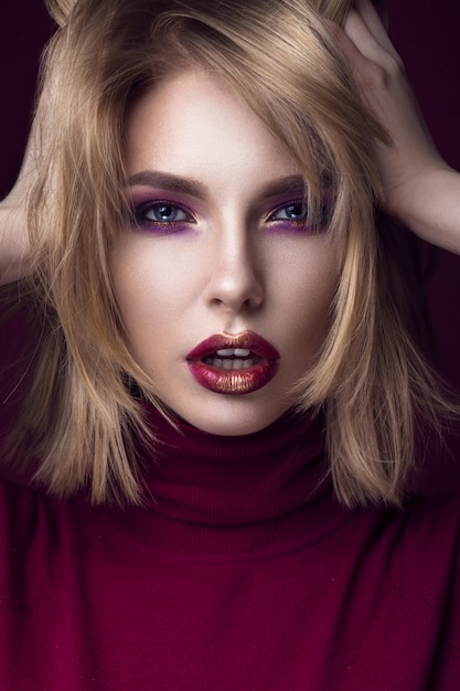 Foto schöne blonde frau in einem roten pullover mit hellem make-up und dunklen lippen.
