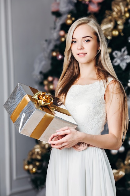 Schöne blonde Frau in einem weißen Kleid mit einem Geschenk