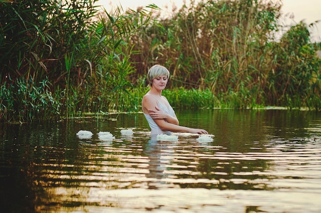 Schöne blonde Frau mit kurzen Haaren schwimmen, entspannen im See bei Sonnenuntergang. Sommerurlaub.