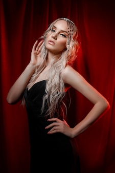 Schöne blonde frau mit langen haaren auf rotem samthintergrund haarschmuck auf dem kopf einer frau, modernes make-up und pfeile auf den augen