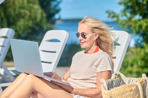 Schöne blonde Frau mit Laptop sitzt in einer Chaiselongue