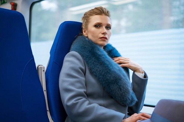 Schöne blonde Frau mit Make-up in einem blauen Mantel reitet im Zug schaut aus dem Fenster