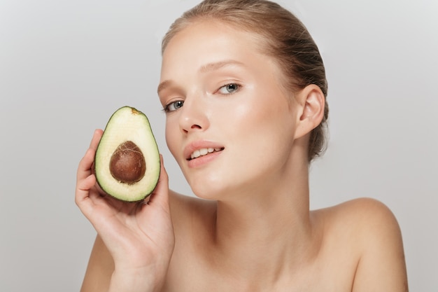 Schöne blonde Frau mit perfekter Haut und einer Avocado