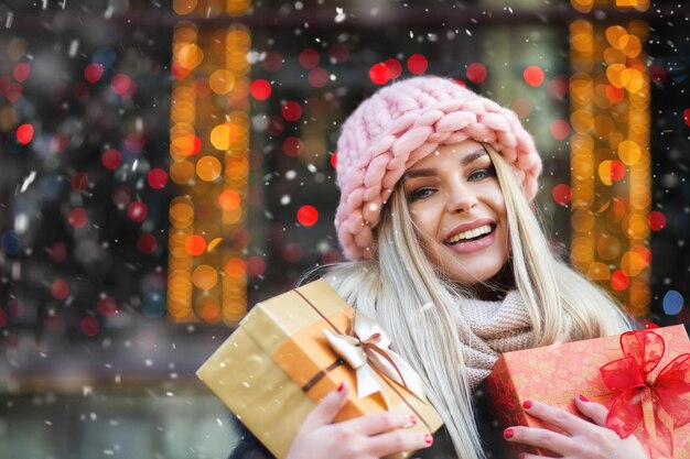 Schöne blonde Frau trägt gestrickte rosa Mütze und genießt Geschenke auf der Wintermesse. Platz für Text