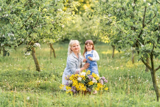 Schöne blonde Frau und ihre kleine Tochter sitzen in einem Frühlingsgarten mit einem großen Blumenkorb