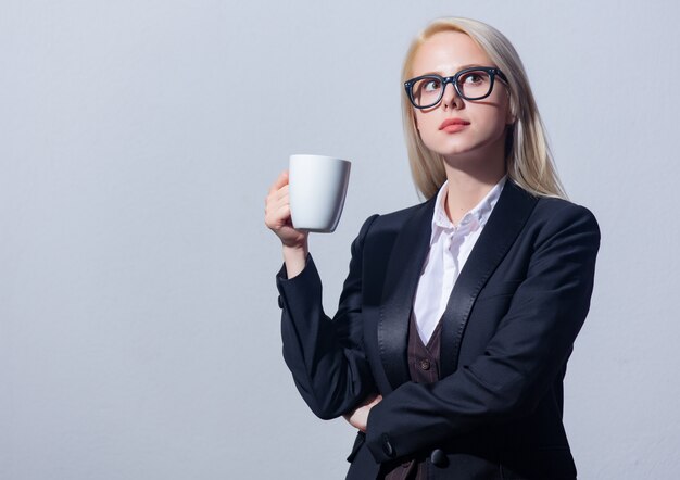 Schöne blonde Geschäftsfrau im Anzug mit Tasse Kaffee