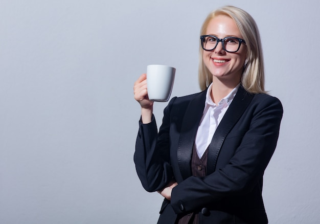 Schöne blonde Geschäftsfrau im Anzug mit Tasse Kaffee