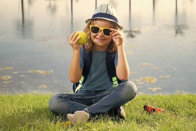 Schöne blonde Kleine mit Fernglas, die einen Entdeckerhut und einen Rucksack in der Natur trägt.