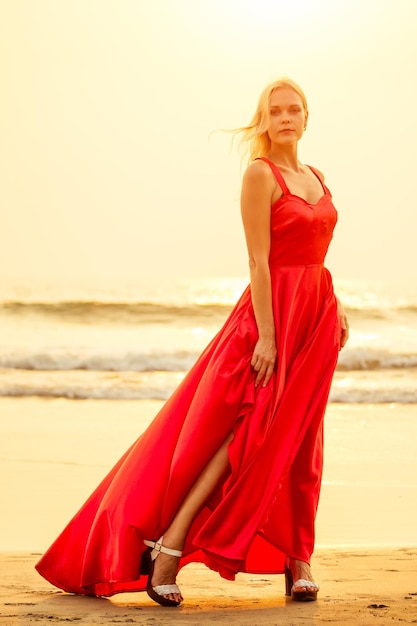 Schöne blonde sinnliche Glamour Leidenschaft Verlangen Sexualität Frau im fliegenden roten Schmetterling Seidenkleid langes Bein und Schuhe mit hohen Absätzen Meer und tropische Insel Sonnenuntergang Hintergrundtango Romantik Valentinstag