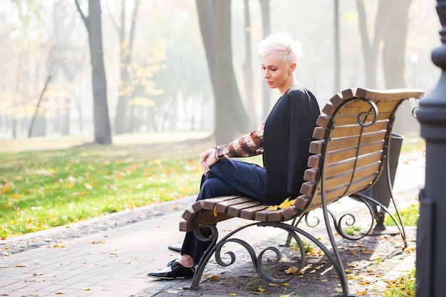 Schöne blonde stilvolle Frau im Herbstpark auf der Bank