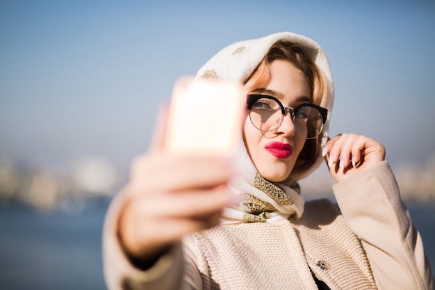 Schöne blonde Touristin, die Selfie auf dem Smartphone macht. Frau trägt Schal und Brille