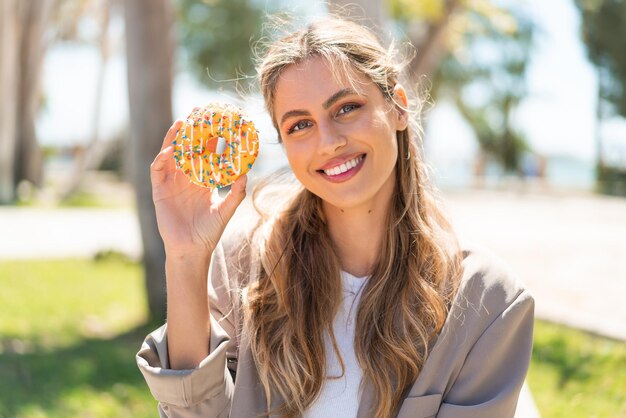 Schöne blonde uruguayische Frau hält einen Donut im Freien und lächelt viel