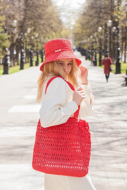Schöne Blondine auf einem Spaziergang mit einer Tasche und einem handgefertigten roten Hut