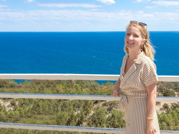 Schöne Blondine, die auf einem Berg mit Blick auf das Meer lächelt. Reisen und Tourismus. Platz kopieren.