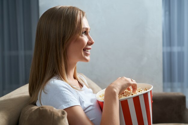 Schöne Blondine, die fernsieht und Popcorn isst