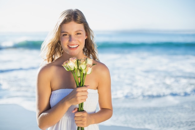 Schöne Blondine in den sundress, die Rosen auf dem Strand halten