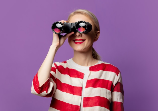 Schöne Blondine in der roten Jacke mit Fernglas auf Pupillenhintergrund