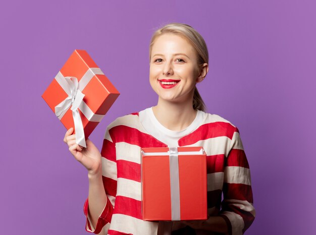 Schöne Blondine in der roten Jacke mit Geschenkbox auf lila Hintergrund