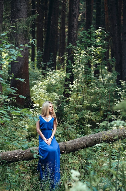 Schöne Blondine in einem langen blauen Kleid im Wald