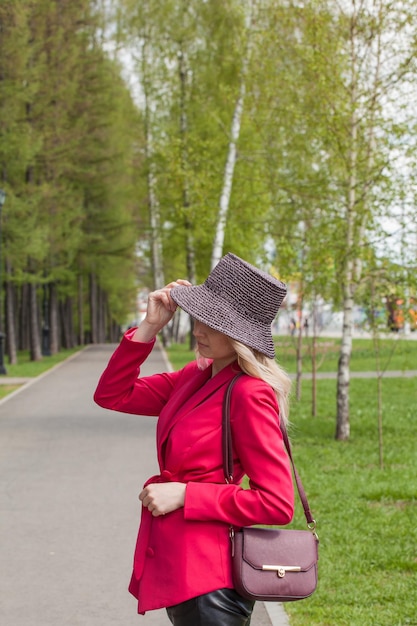 Schöne Blondine in einer roten Jacke und einem Hut im City-Stil