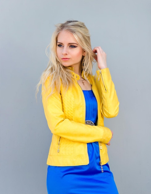 Foto schöne blondine in gelber jacke und blauem kleid im studio