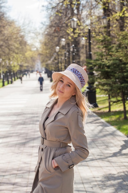 Schöne Blondine in Regenmantel und Hut bei einem Spaziergang im Park