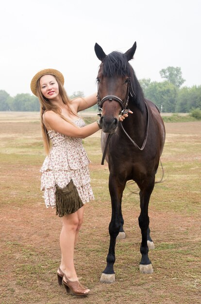 Schöne Blondine in Strohhut und Sommerkleid mit Pferd fotografiert