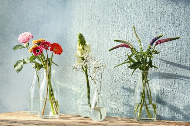 Schöne Blumen in Glasvasen auf Holztisch und strukturierter Wand