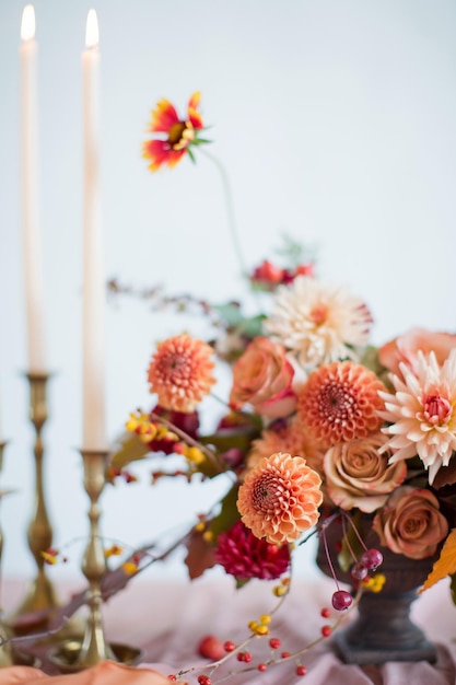 Schöne Blumenkomposition mit orangefarbenen und roten Herbstblumen und Beeren Herbststrauß in Vintage-Vase auf einem Holztisch mit rosa Gewebe und Kerzen